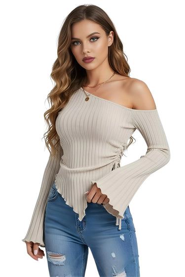 Woman wearing a beige off-shoulder ribbed asymmetrical top and blue jeans on a white background